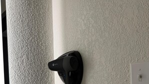 Ein Fön an einer strukturierten Wand in der Nähe eines Fensters, verbunden mit einer Steckdose.