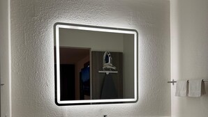 Ein Badezimmer mit weißem Waschbecken, einem Spiegel mit beleuchtetem Rahmen und einem Handtuchhalter.