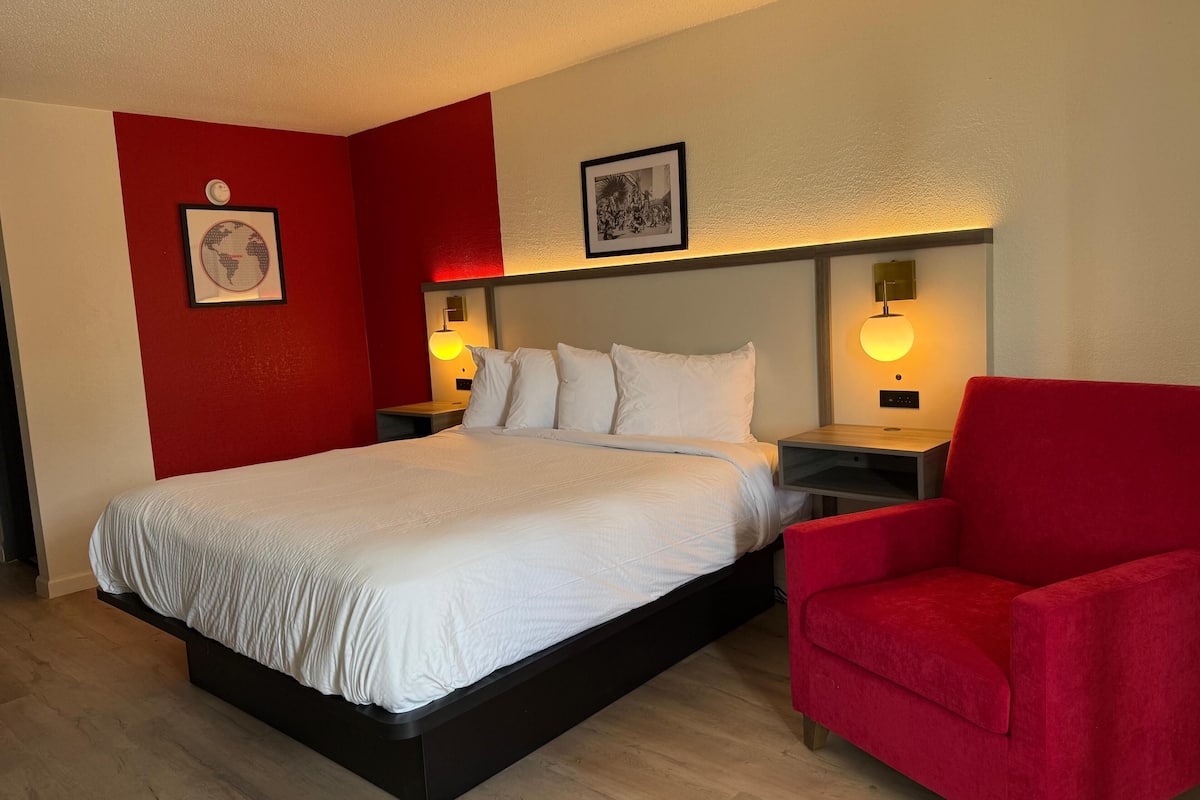 A hotel room with a large bed, a red armchair, and two bedside lamps.
