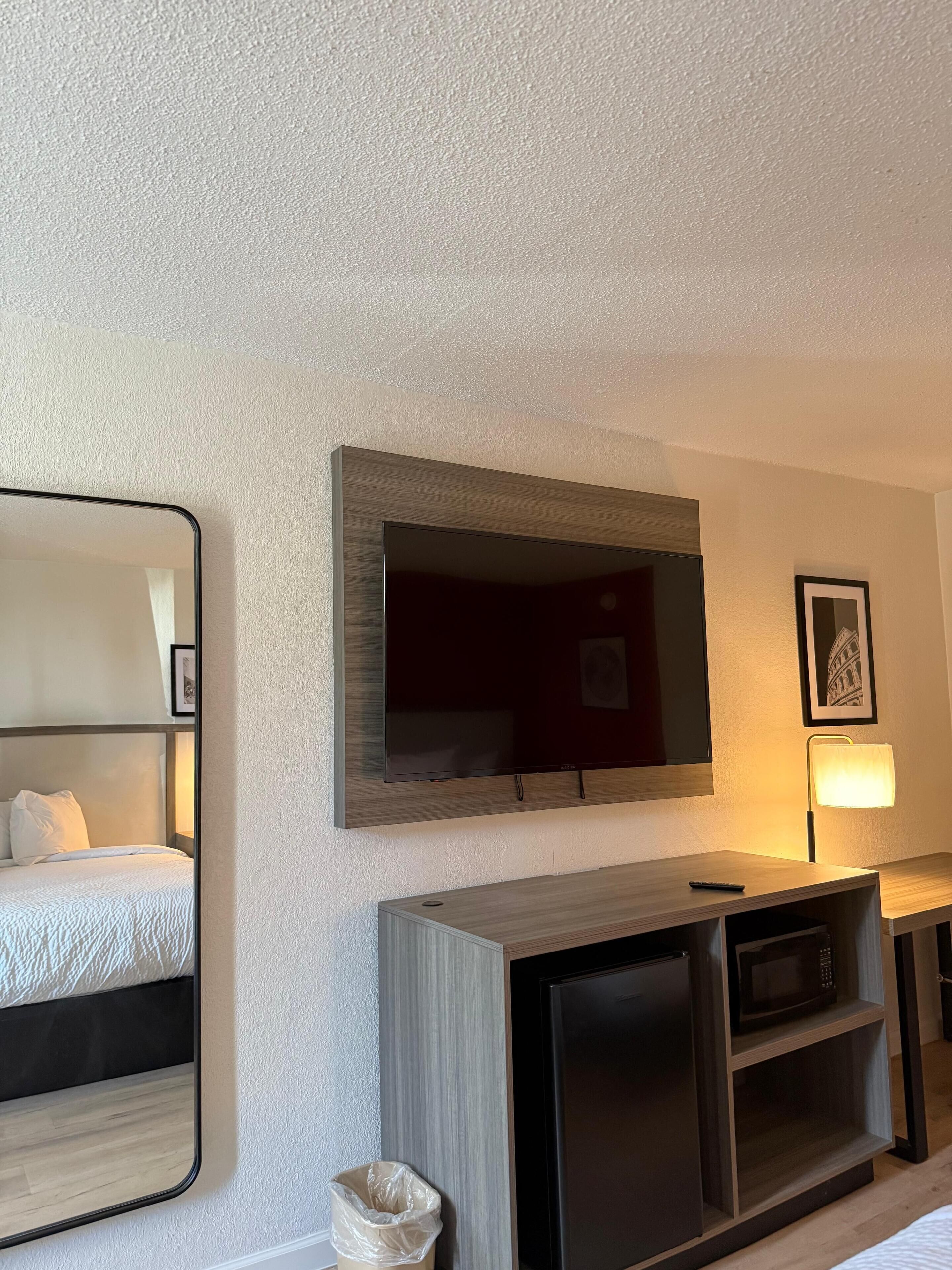 Een hotelkamer met een bed, een aan de muur bevestigde televisie, een houten kast en een prullenbak.
