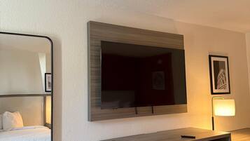 Een hotelkamer met een bed, een aan de muur bevestigde televisie, een houten kast en een prullenbak.