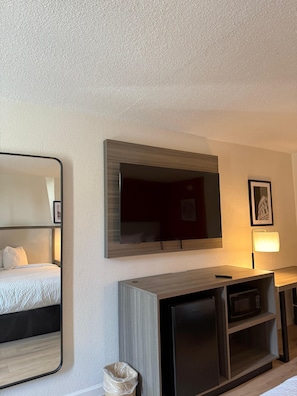 A hotel room with a bed, a TV mounted on the wall, a wooden cabinet, and a trash bin.