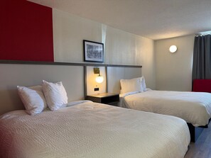 A hotel room with two beds, a bedside table with a lamp, a framed picture on the wall, and a red accent wall. - Ramada by Wyndham Lumberton NC North (Lumberton)