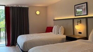 Ein Hotelzimmer mit zwei Betten, einer roten Akzentwand, einer runden Wandleuchte und einem gerahmten Bild an der Wand.
