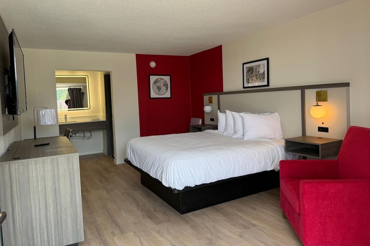 A hotel room with a bed, a desk, a chair, a TV, and a red accent wall.