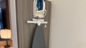 Ein Zimmer mit Schreibtisch aus Holz, einer Lampe und einem Bügeleisen an einem Wandgestell.