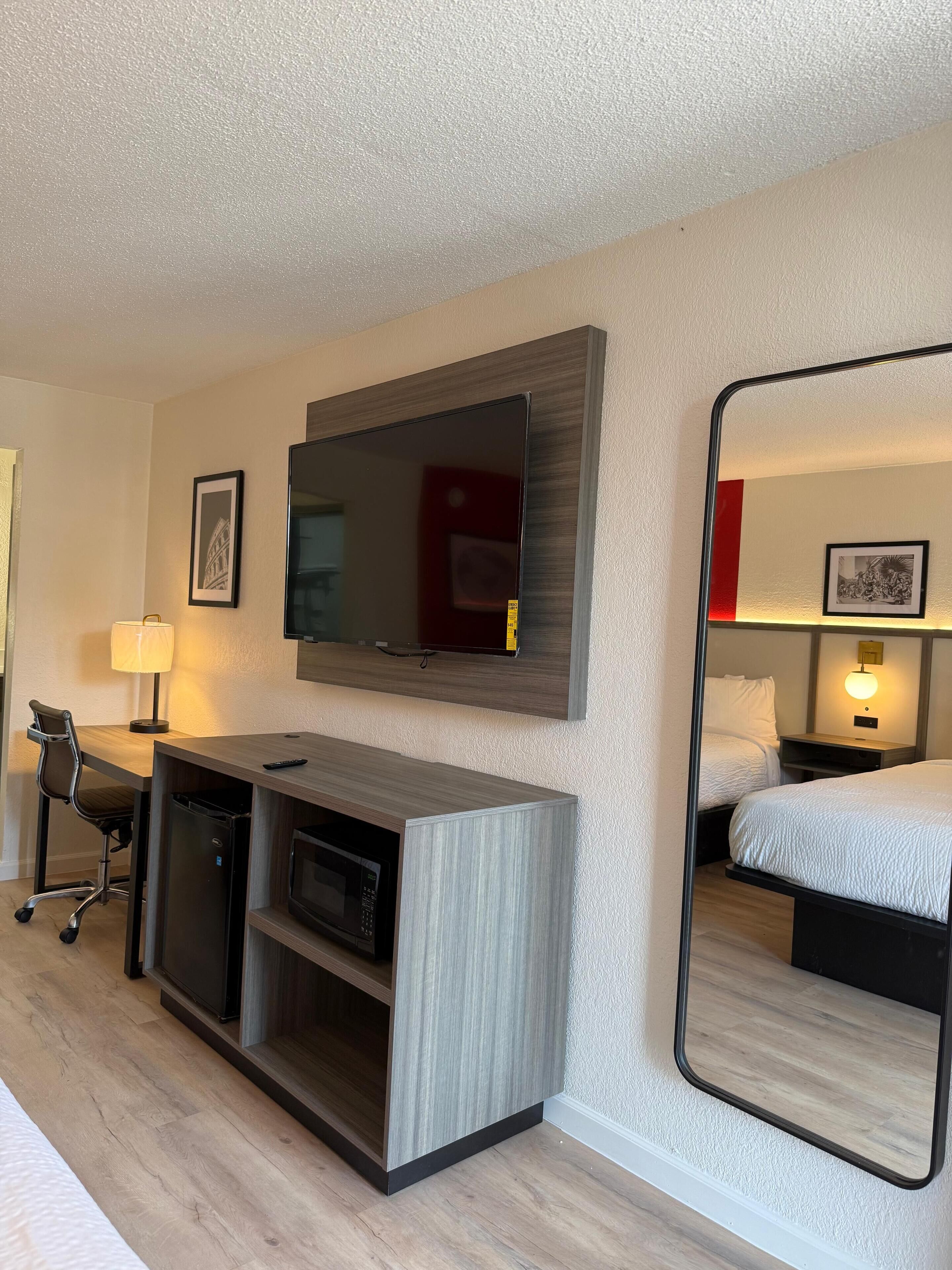 A hotel room with a desk, chair, TV, and a bed.