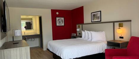 A hotel room with a bed, a desk, a chair, a TV, and a red accent wall.