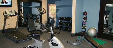 A gym with treadmills, an elliptical, a bench press, dumbbells, and a stationary bike.