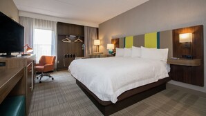 A hotel room with a large bed, a desk with a television, a chair, and a desk lamp.