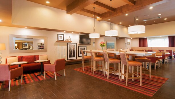A modern hotel lobby with a dining area, red seating, and wooden accents. - Hampton Inn Brevard (Pisgah Forest)