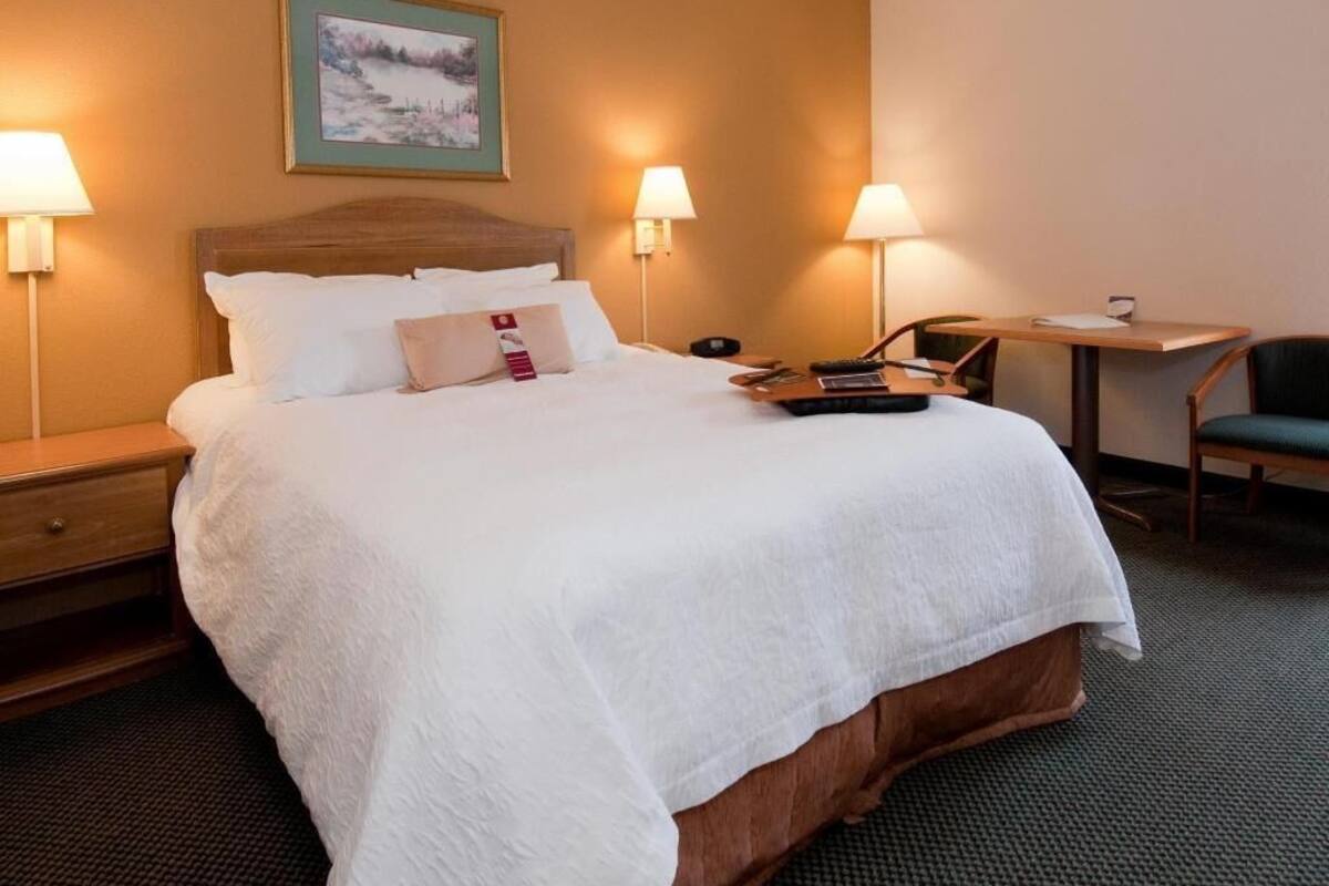 A hotel room with a bed, bedside lamps, a desk, and a chair.