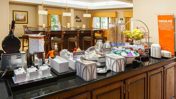 Un bufé de desayuno de hotel con diversas estaciones de comida, incluyendo un bol de fruta y una estación de café.