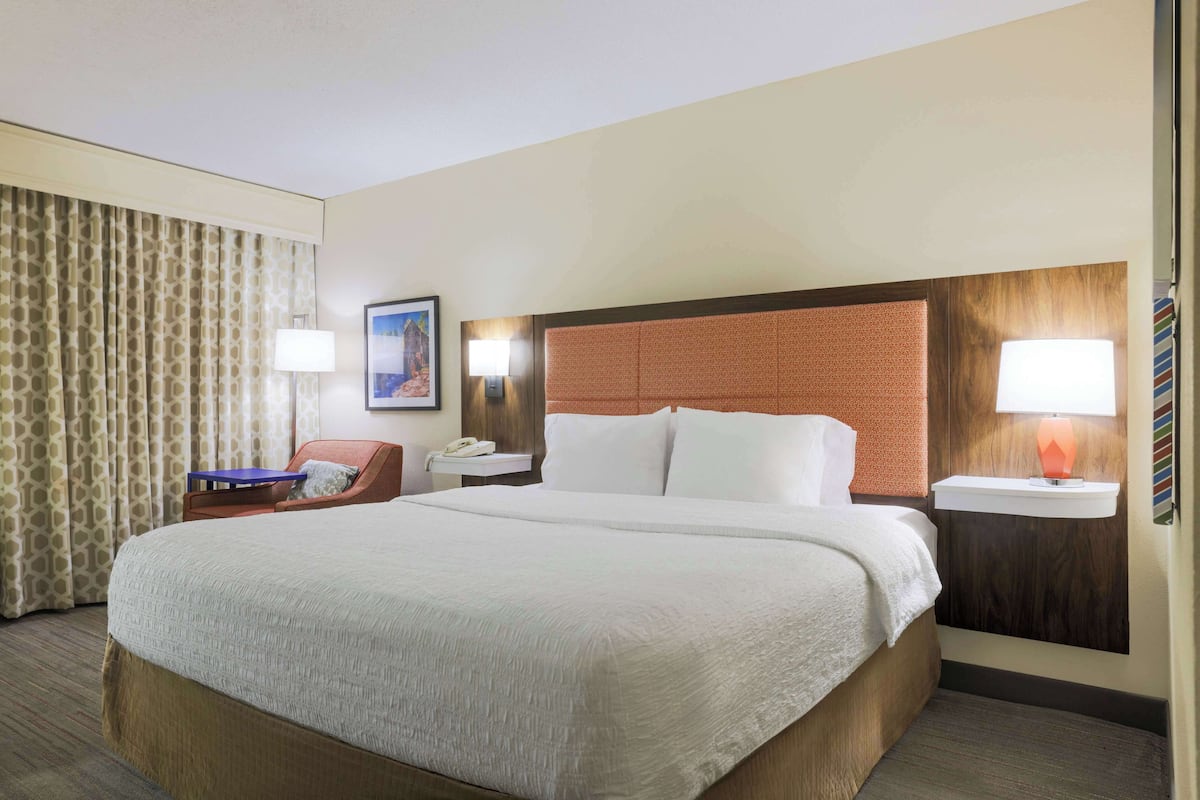 Habitación de hotel con una cama grande, un escritorio con lámpara, una silla y un cuadro en la pared.