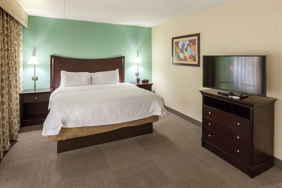 Una habitación de hotel con cama, lámparas de noche, televisor y cómoda.