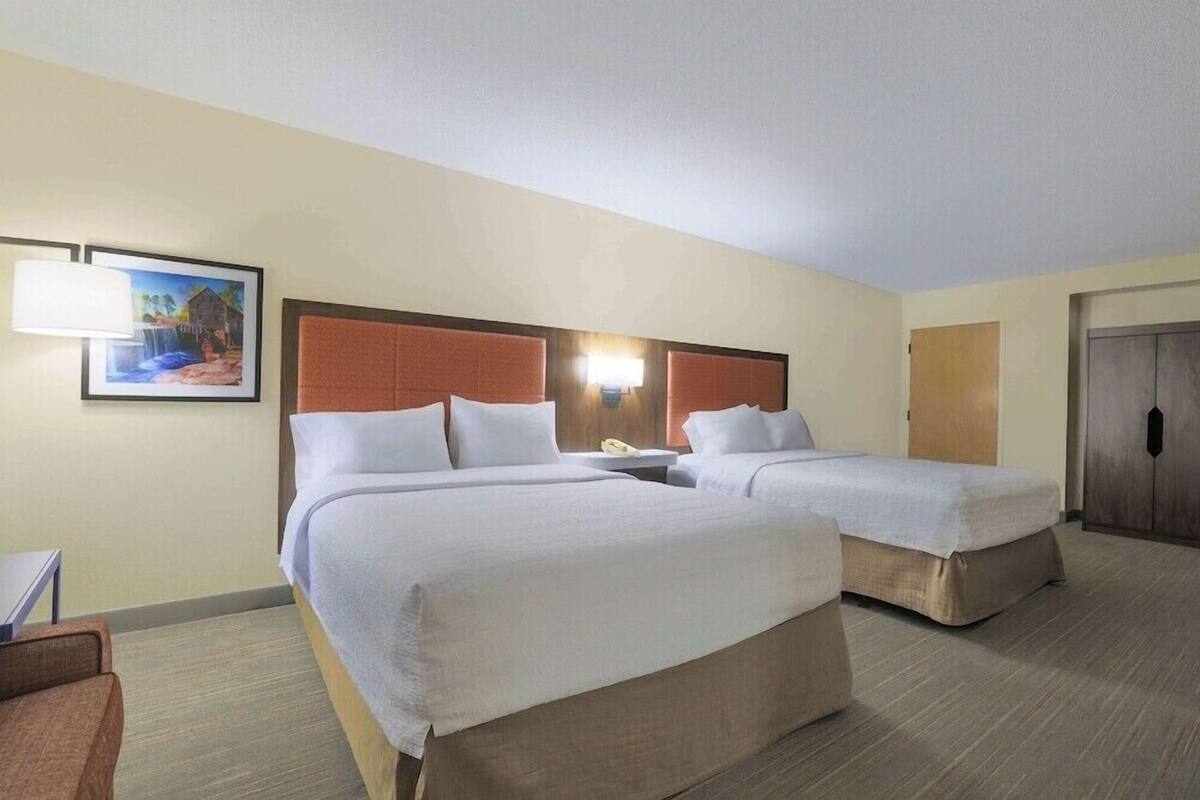 Una habitación de hotel con dos camas, una mesita de noche, una lámpara y un cuadro en la pared.