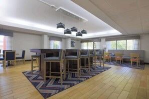 A spacious room with a high ceiling, a central bar area with stools, a sofa, and a patterned rug. - Hampton Inn Raleigh Garner (Garner)