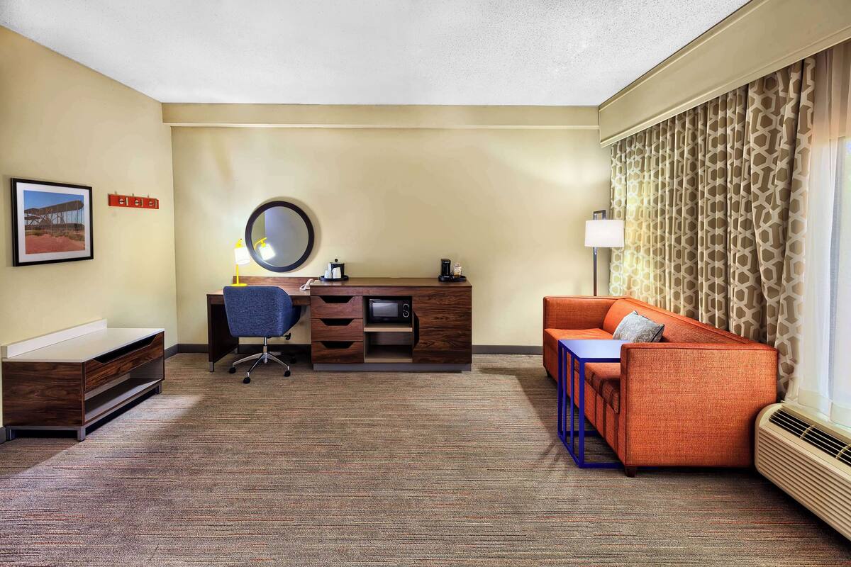 Una habitación de hotel con escritorio, silla y sofá naranja.