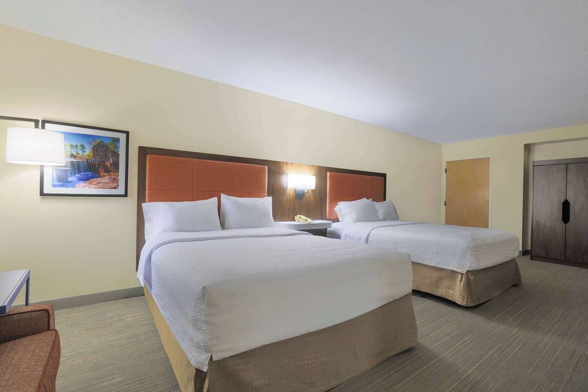 Habitación de hotel con dos camas, una mesita de noche, una lámpara y un cuadro en la pared.