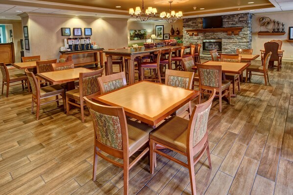 A spacious dining area with wooden tables and chairs, a stone fireplace, and a coffee bar with multiple dispensers.