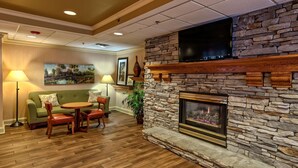 A cozy living area with a stone fireplace, a flat-screen TV mounted above it, a green sofa with patterned cushions, and a wooden coffee table. - Hampton Inn by Hilton Concord/Kannapolis (Concord)