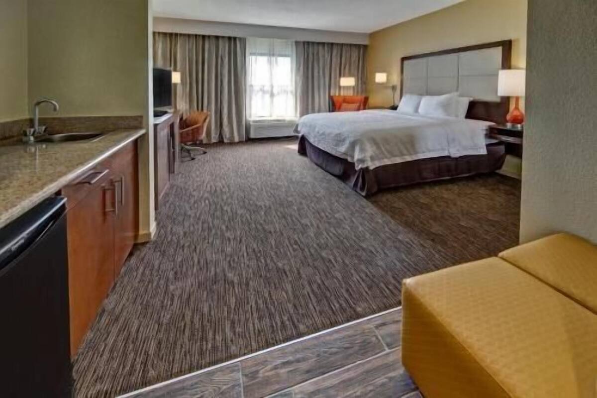 A hotel room with a bed, a desk with a chair, a sofa, and a bathroom with a sink and mirror.