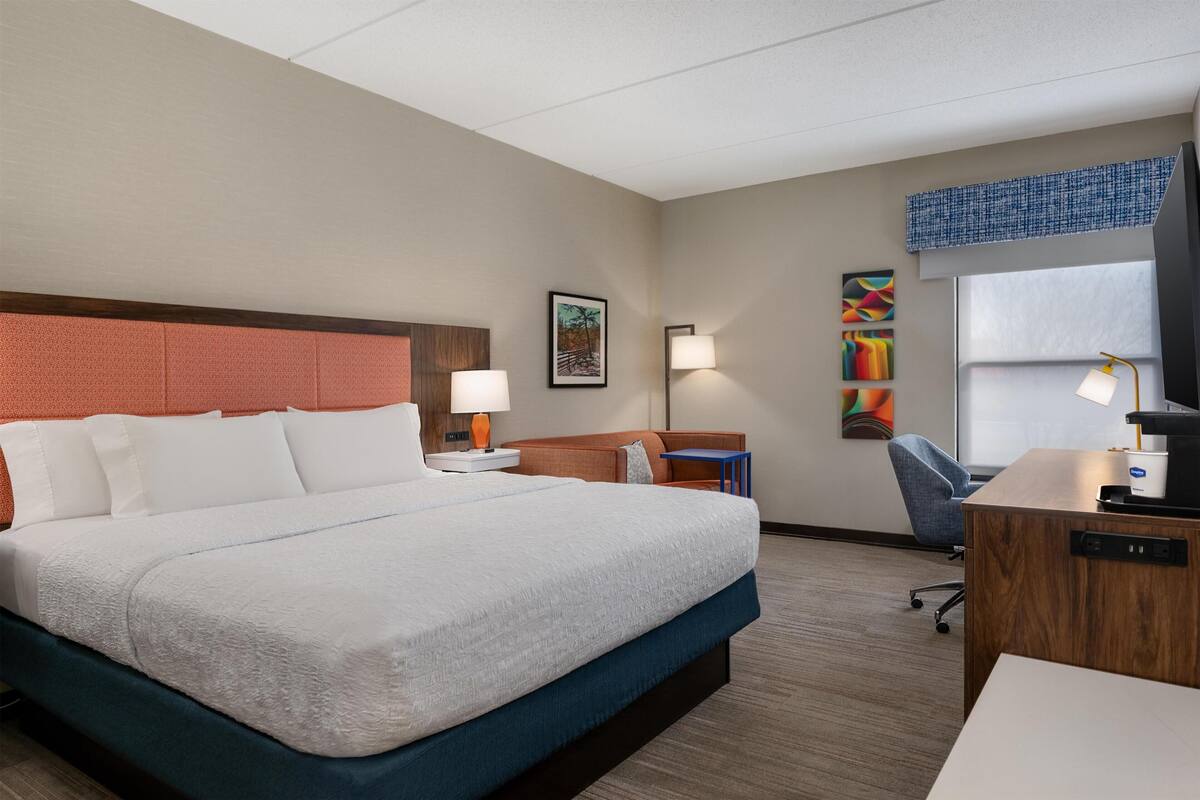 A hotel room with a bed, desk, chair, and artwork on the walls.