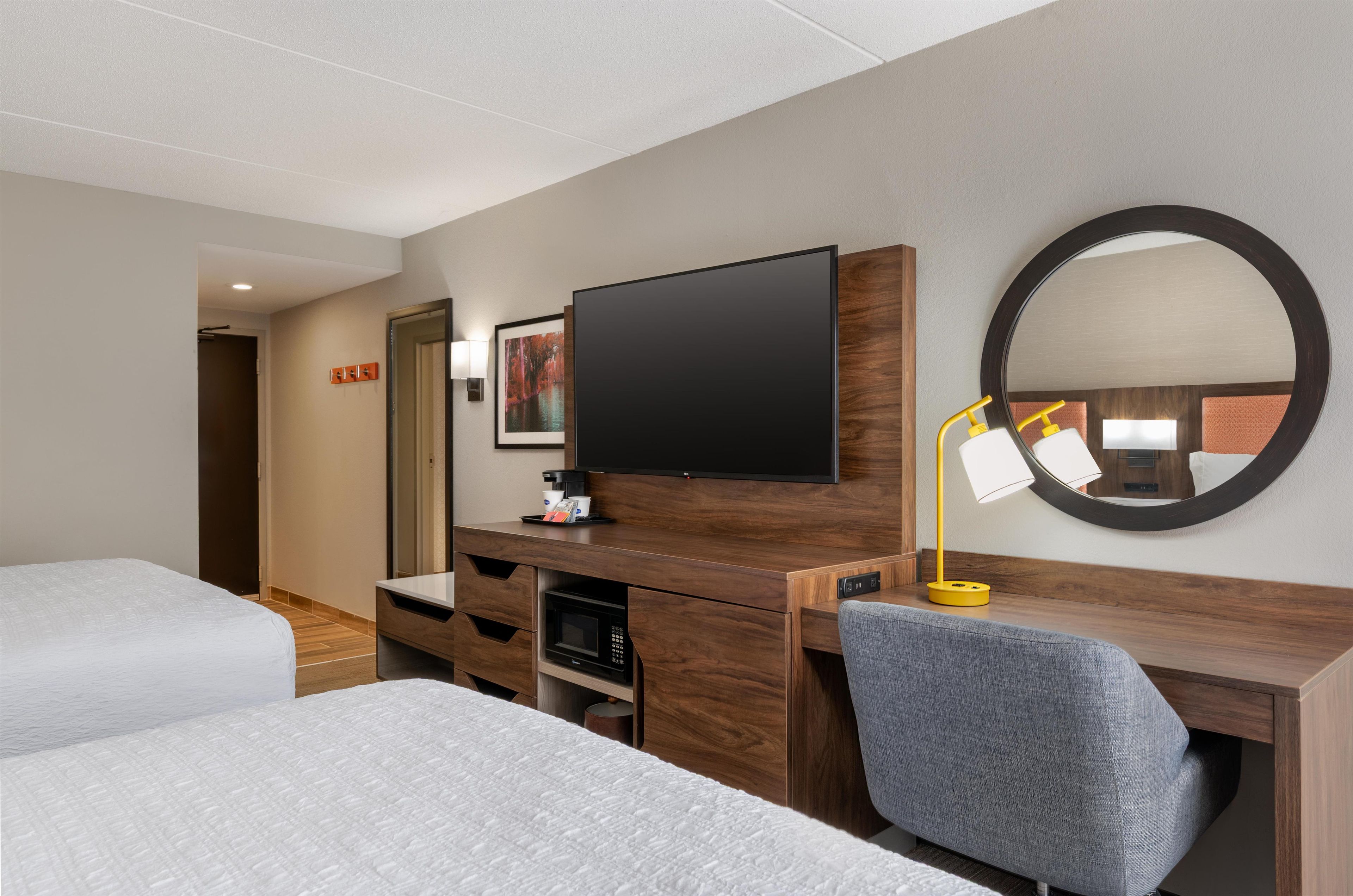 Une chambre d’hôtel avec deux lits, une télévision, un bureau avec un miroir et une machine à café.