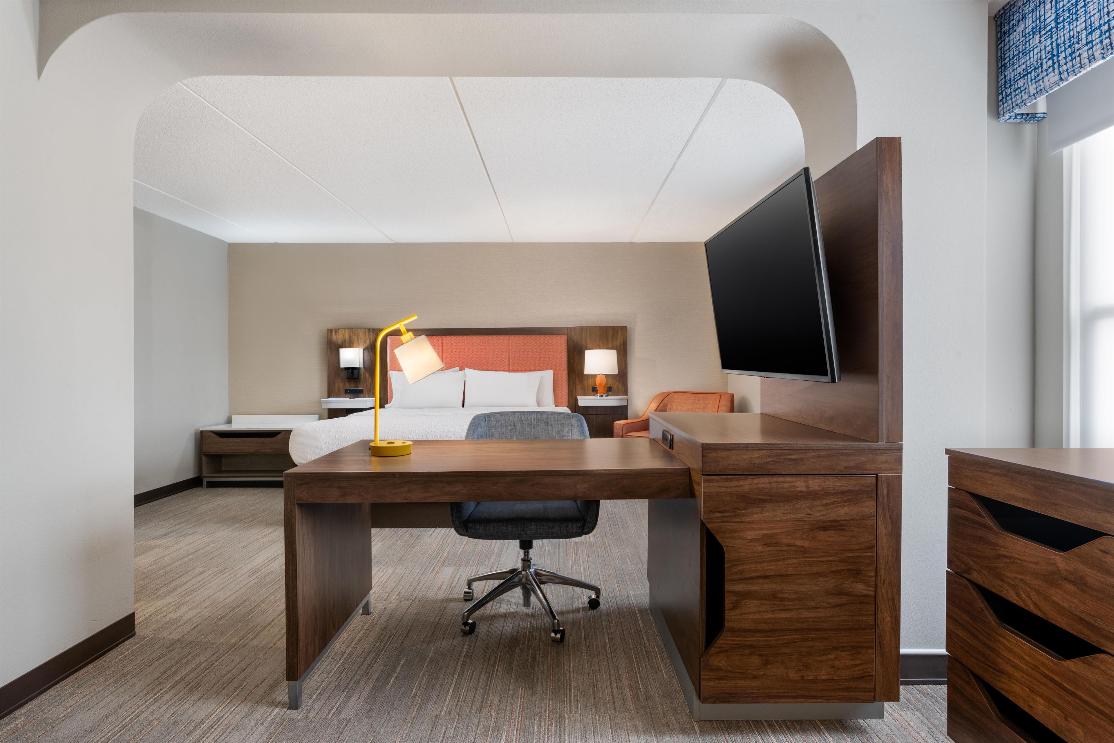 Una habitación de hotel con escritorio, silla, cama, mesitas de noche, lámparas y televisión.