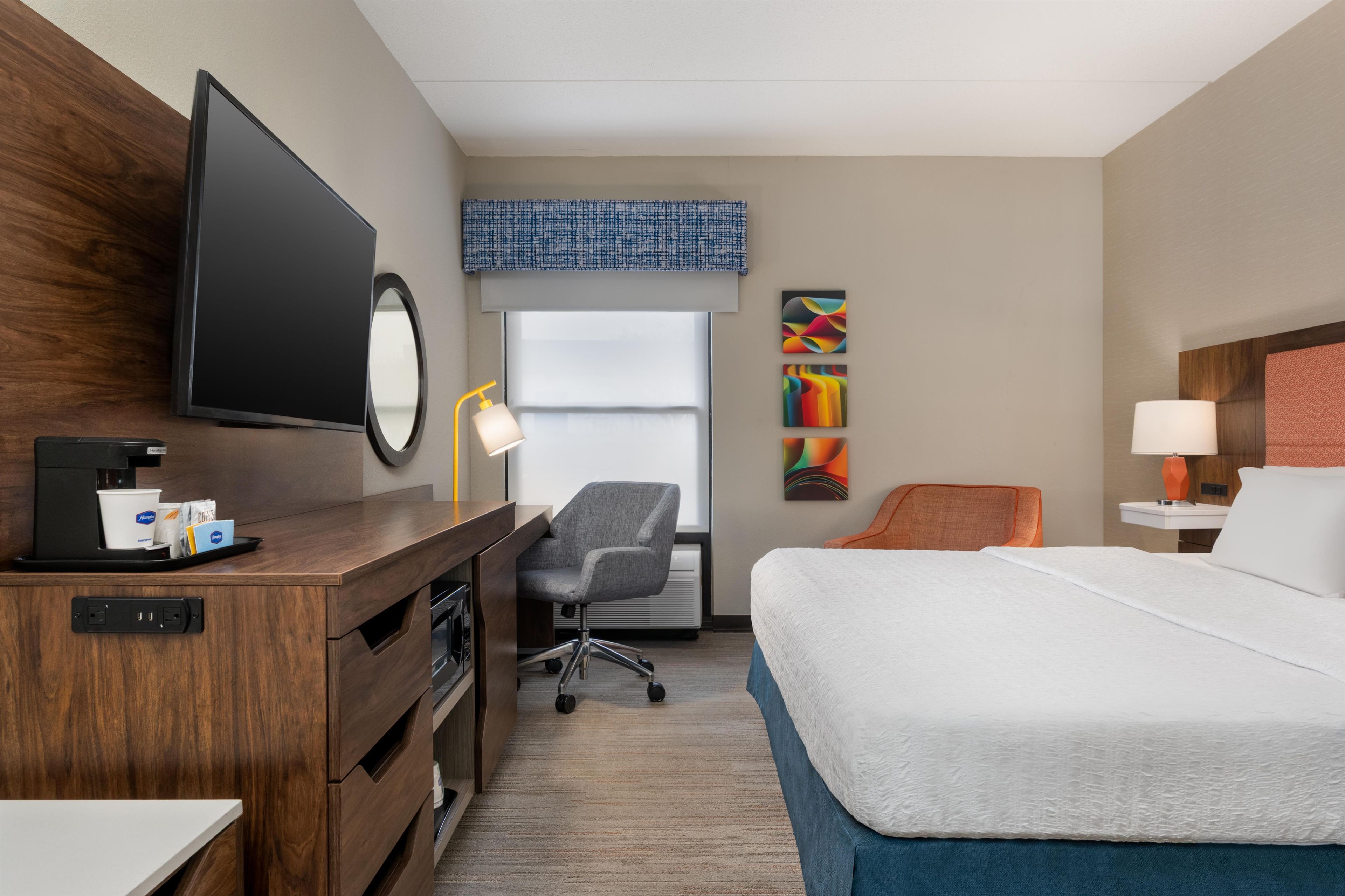 A hotel room with a bed, desk, chair, and a television.