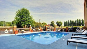 Ein Swimmingpool mit Liegestühlen und einem Zaun, umgeben von Bäumen und einem klaren Himmel.
