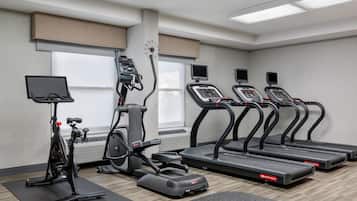 Un gimnasio con cintas de correr, elípticas y una bicicleta estática.