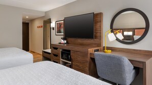 Ein Hotelzimmer mit zwei Betten, einem Schreibtisch, einem Fernseher, einem Spiegel und einer Mikrowelle.