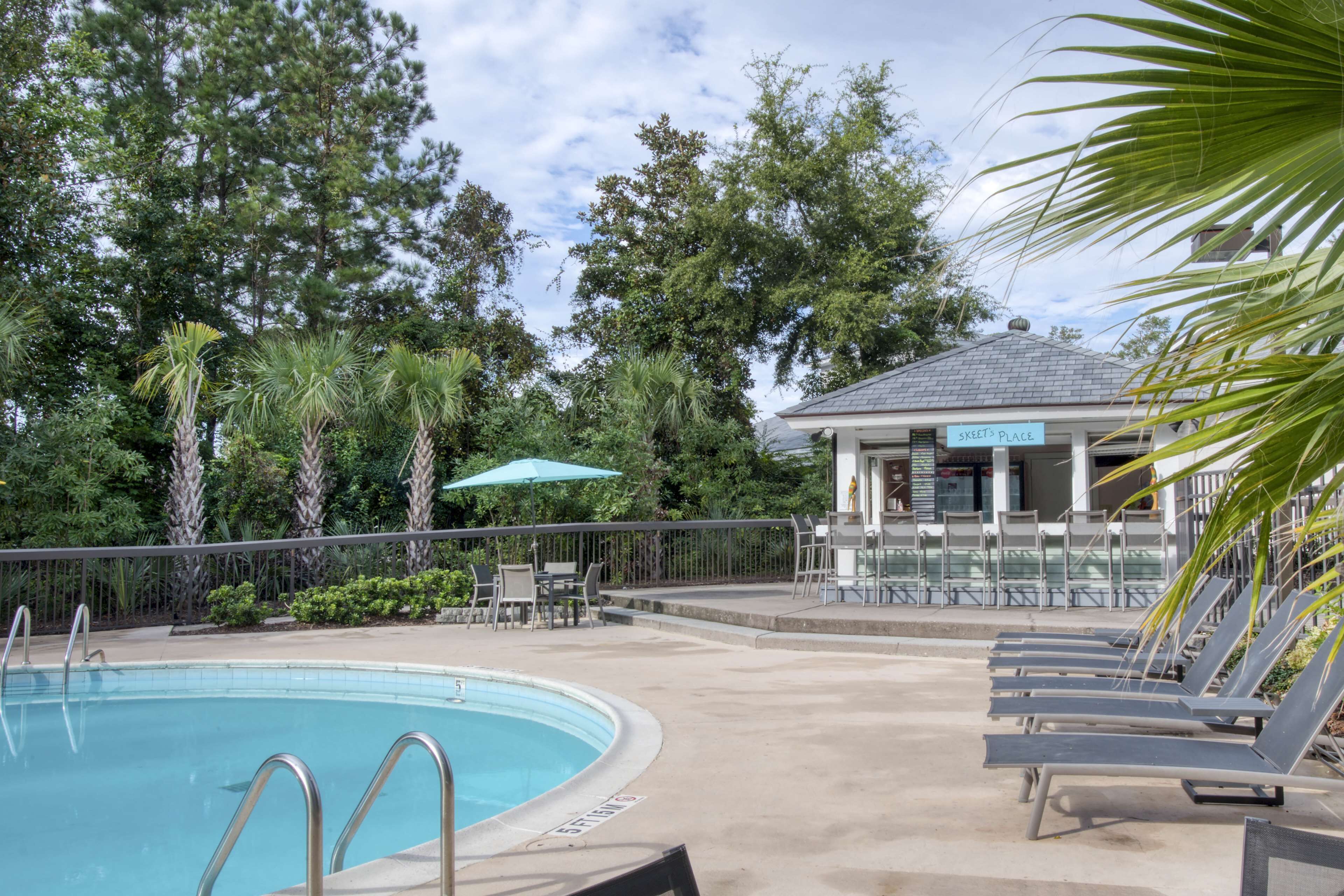 Uma piscina com área de estar, um gazebo e vegetação ao redor.