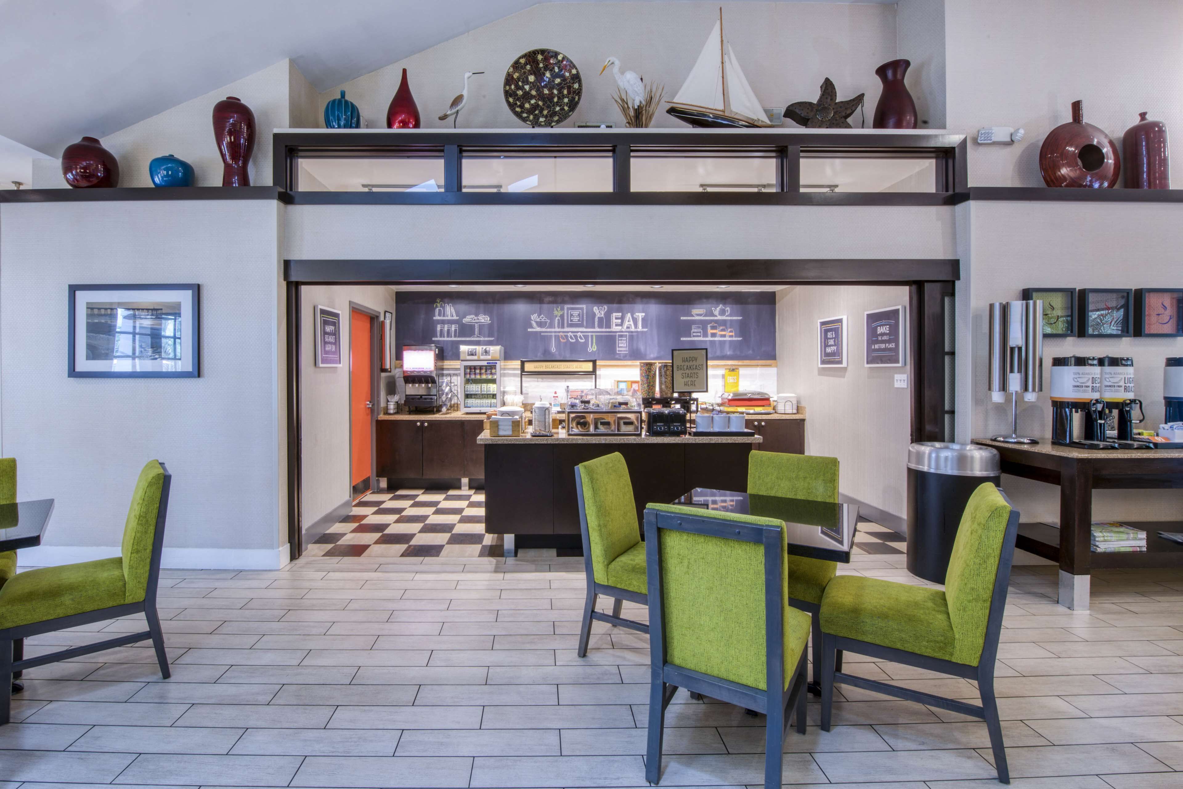 Un restaurant avec un sol à carreaux, des chaises vertes et un comptoir où le menu est écrit sur un tableau noir.