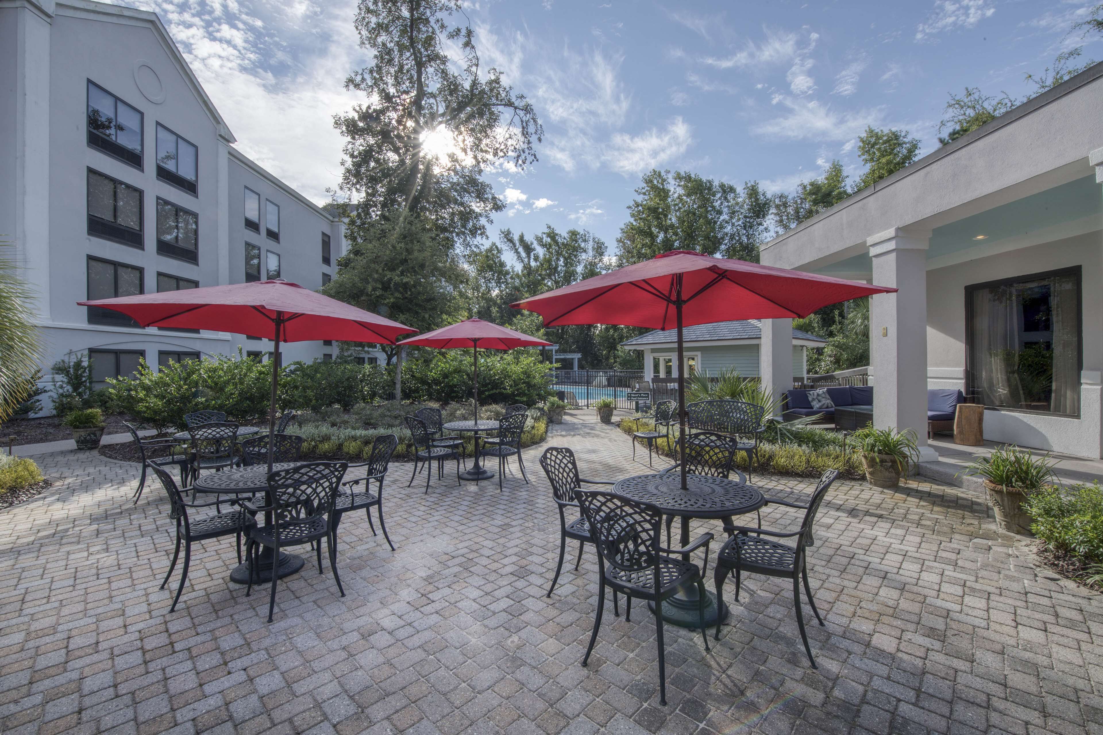 A courtyard with outdoor seating, red umbrellas, and a pool in the background.