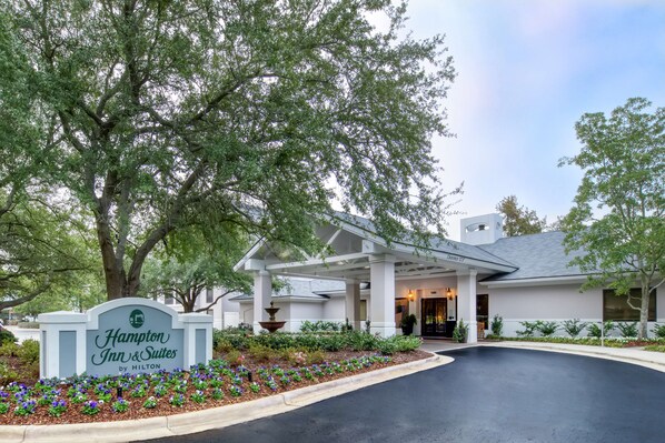 A Hampton Inn & Suites by Hilton with a covered entrance, landscaped garden, and a fountain.