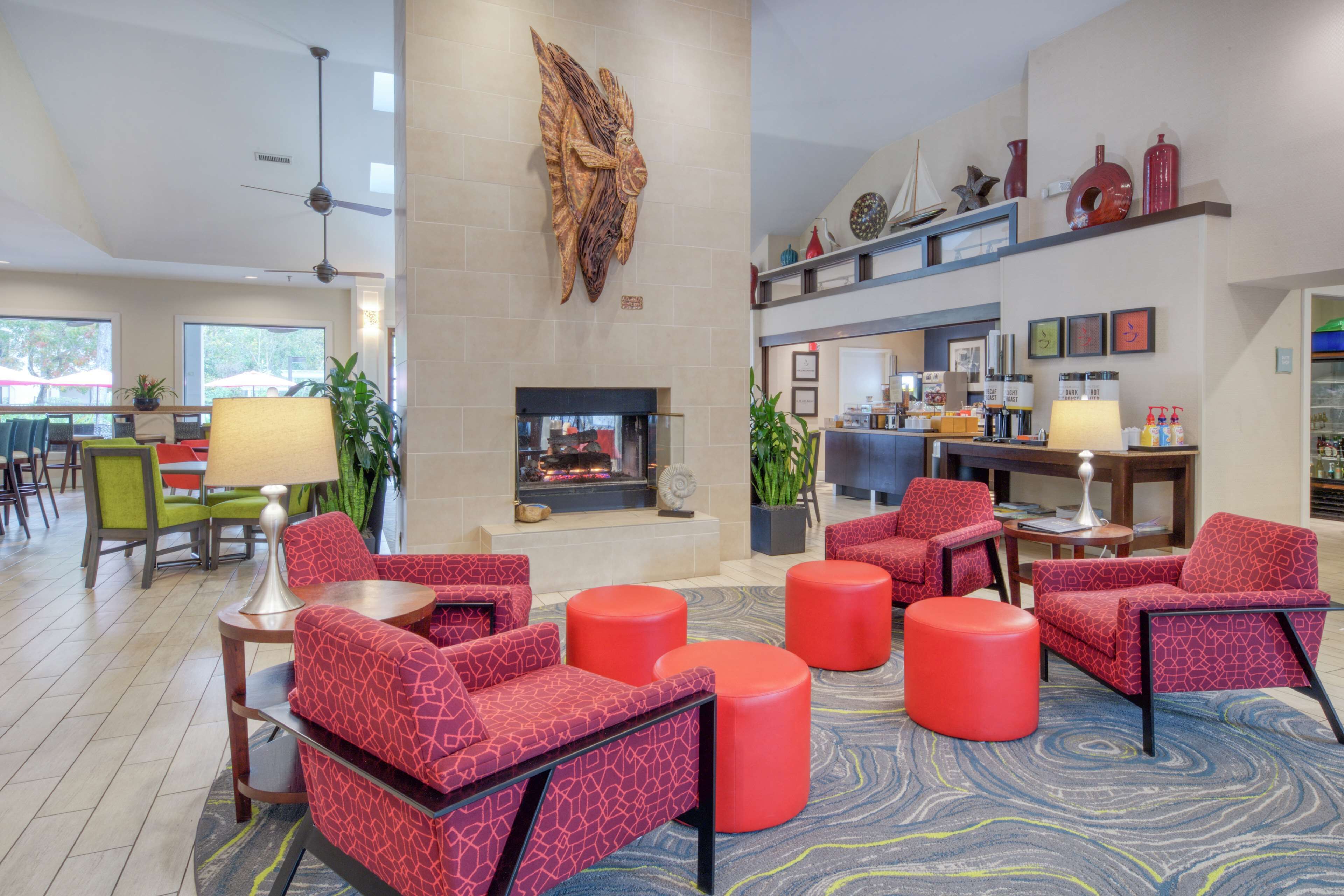 A spacious lobby with red patterned seating, a fireplace, and a coffee bar.