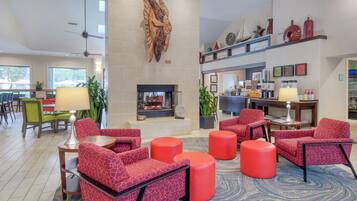 A spacious lobby with red patterned seating, a fireplace, and a coffee bar.