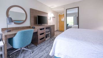 Quarto de hotel com cama, escrivaninha com cadeira, televisão e espelho.