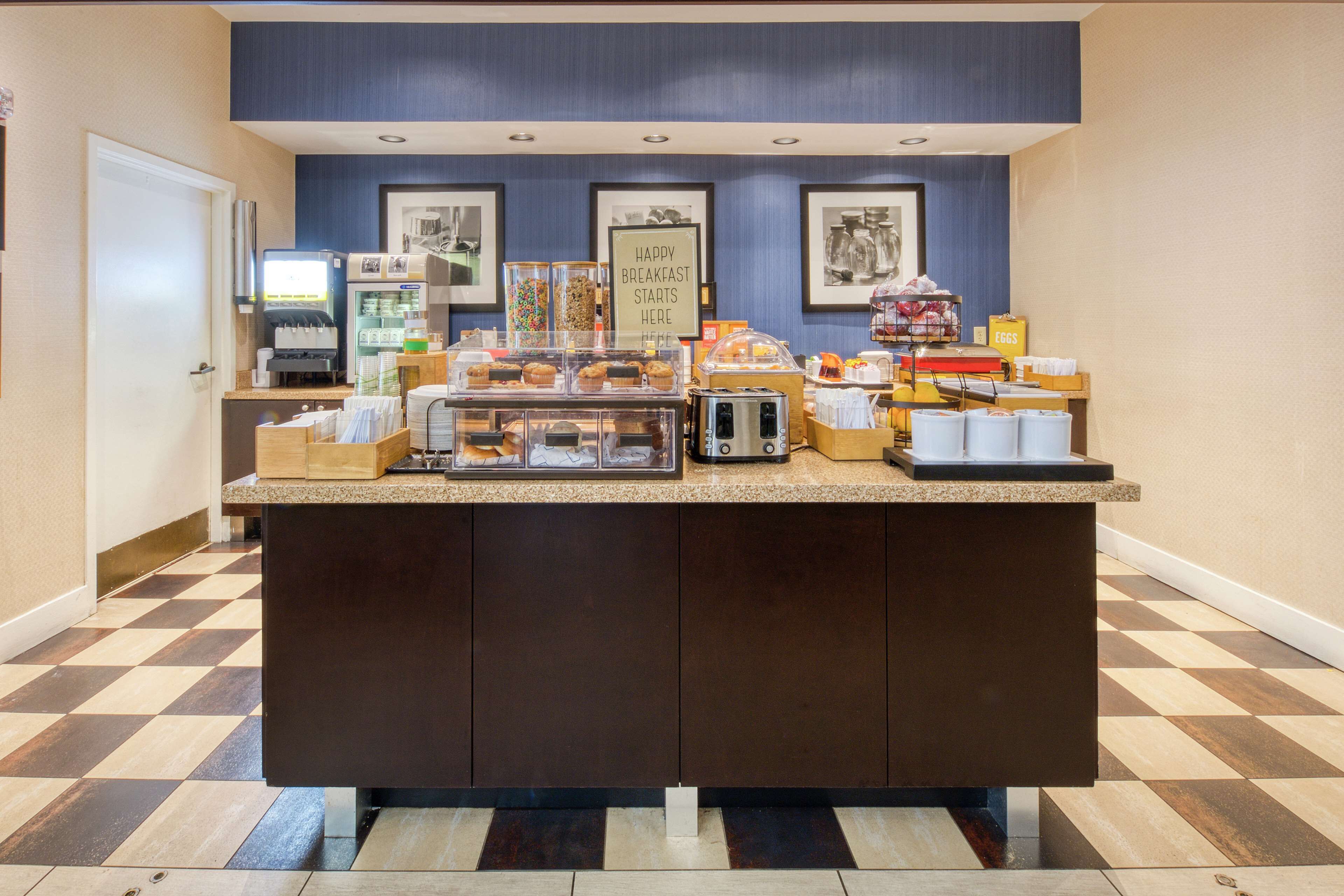 A breakfast bar with a coffee machine, muffin display, and a sign that reads "HAPPY BREAKFAST STARTS HERE".