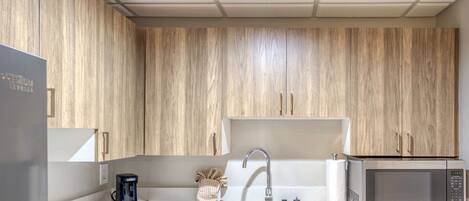 A modern kitchen with wooden cabinets, a stainless steel sink, a coffee maker, a microwave, and a built-in oven.