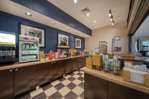 A hotel kitchen with a checkered floor, a refrigerator with food items, and a display case with pastries.