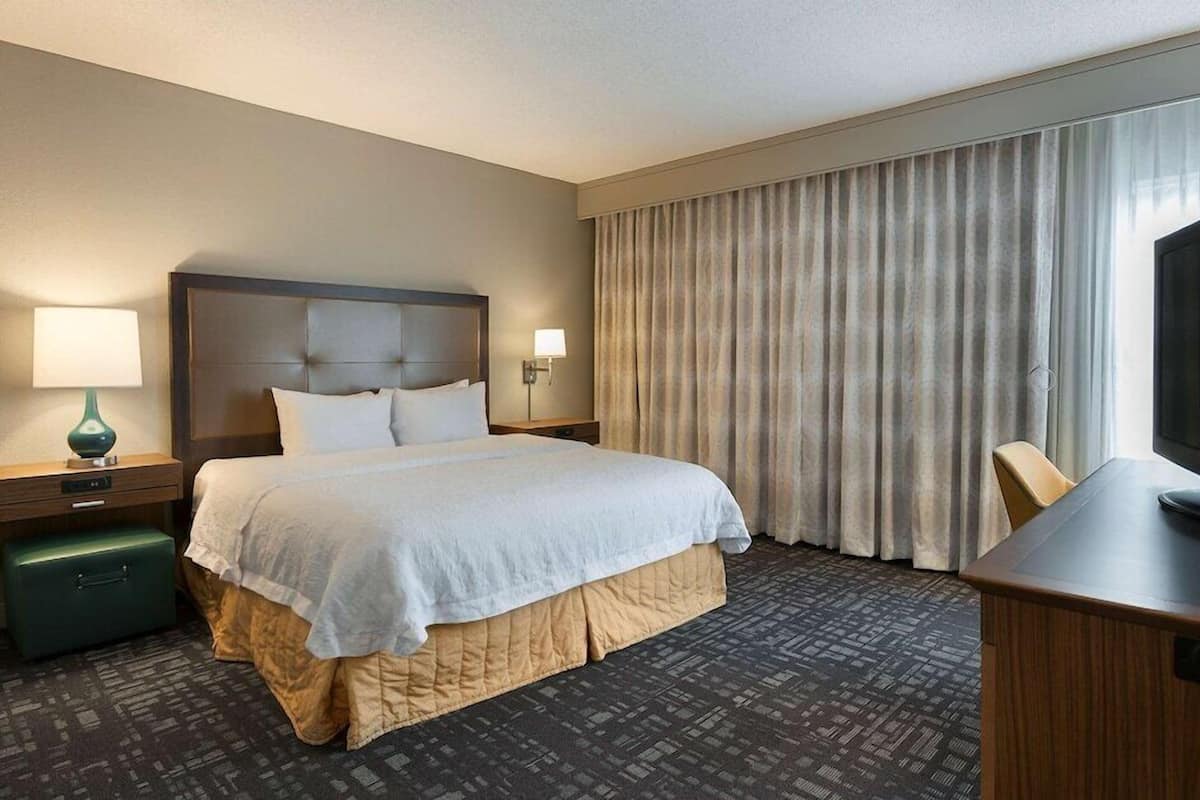 A hotel room with a bed, a desk, a television, a lamp, and a window with curtains.