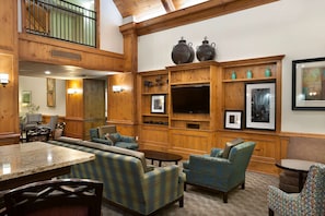 A spacious lobby with a high ceiling, wooden paneling, a seating area with plaid sofas, a dining table, and a TV mounted on the wall. - Hampton Inn & Suites Charlotte/Pineville (Pineville)