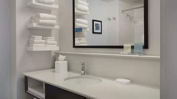 A modern bathroom with a white sink, a large mirror, and shelves holding white towels.