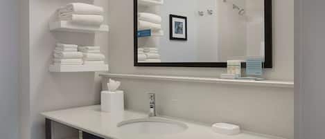 Un baño moderno con un lavabo blanco, un espejo grande y estantes con toallas blancas.