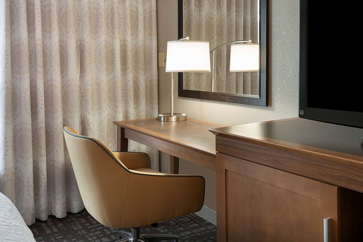 A hotel room with a wooden desk, a chair, a mirror, and a flat-screen TV.