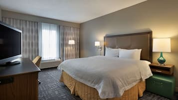 A hotel room with a large bed, a television on a desk, and a green suitcase.