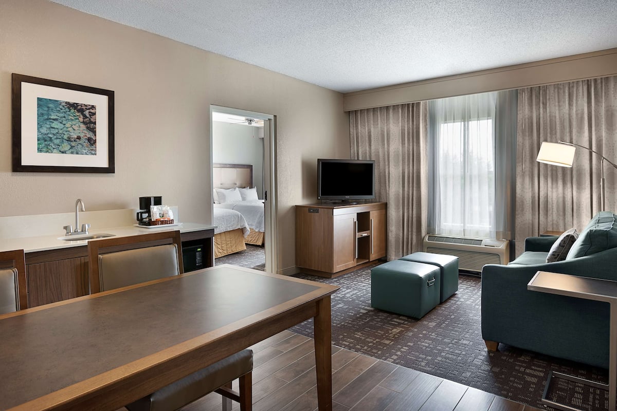 A hotel room with a dining area, a TV, a sofa, and a large window with curtains.